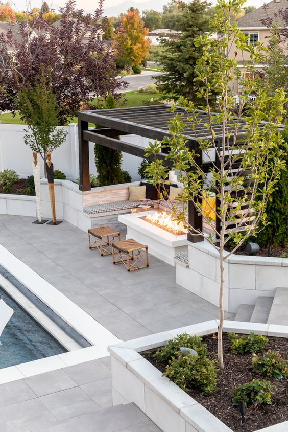 dark stain wood pergola with a large rectangular fire pit with built in seating around it